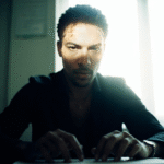 Pessoa adulta em escritório moderno pausando conscientemente com as mãos sobre teclado, expressão facial de reflexão ativa, iluminação natural realçando momento de decisão consciente